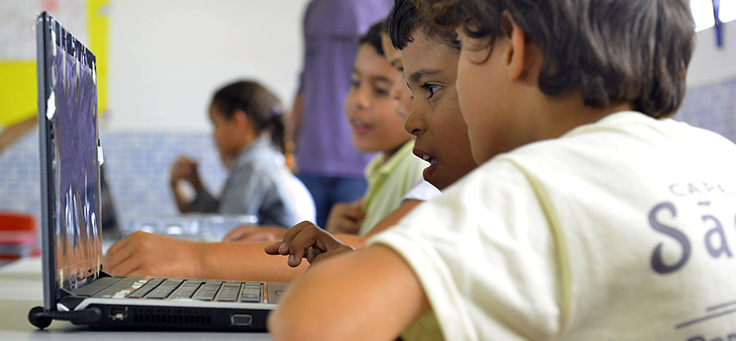 Duas crianças olham para a tela de um computador em sala de aula