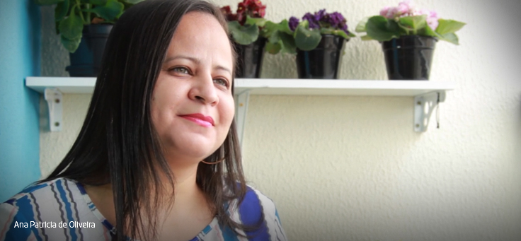 Moça de blusa azul e branca olha para a câmera na frente de vasos de flores.