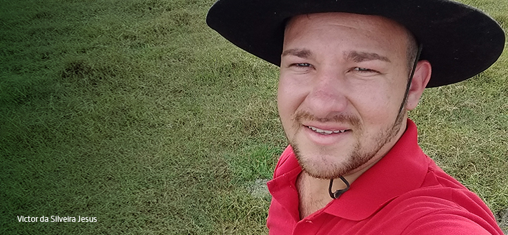 Rapaz de camisa vermelha e chapéu sorri para a câmera em um gramado
