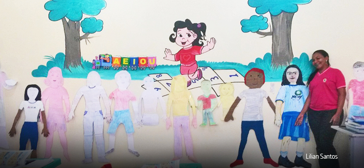 Professora de camiseta rosa posa em frente à parede com desenhos infantis