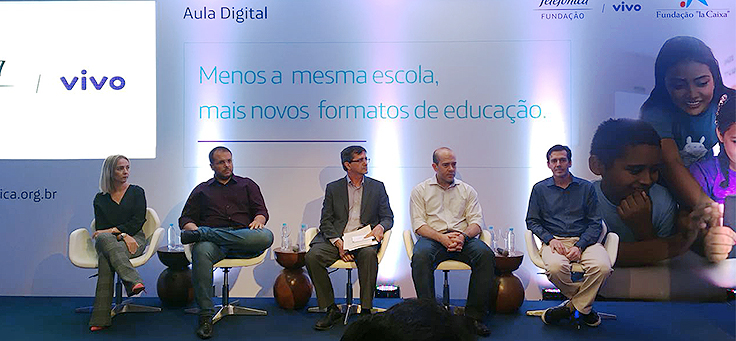 Representantes da Fundação Telefônica Vivo e da Secretaria Estadual de Educação de Sergipe em palco com iluminação reduzida e azulada para apresentação do projeto aula digital