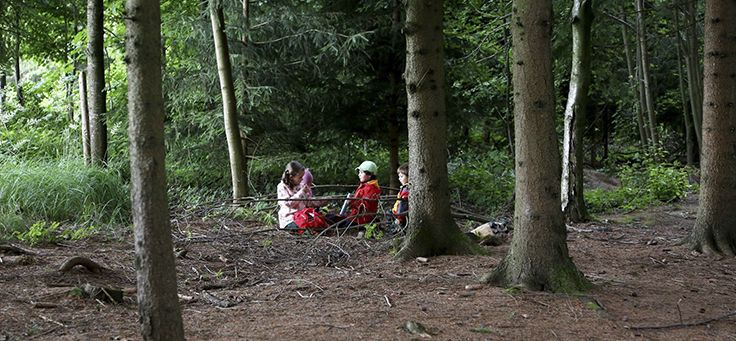 Três crianças brincam em meio a árvores em uma floresta na Alemanha.