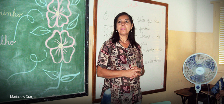 Professora está em frente a lousa onde há uma flor desenhada