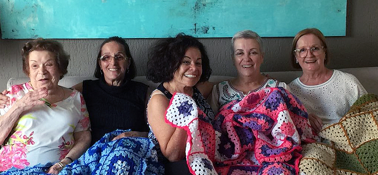Margarete, a segunda da direita para a esquerda, e suas amigas seguram manta feita com os quadrinhos de lã