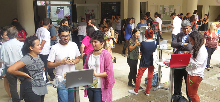 Foto mostra vários grupos de jovens conversando em volta de computadores