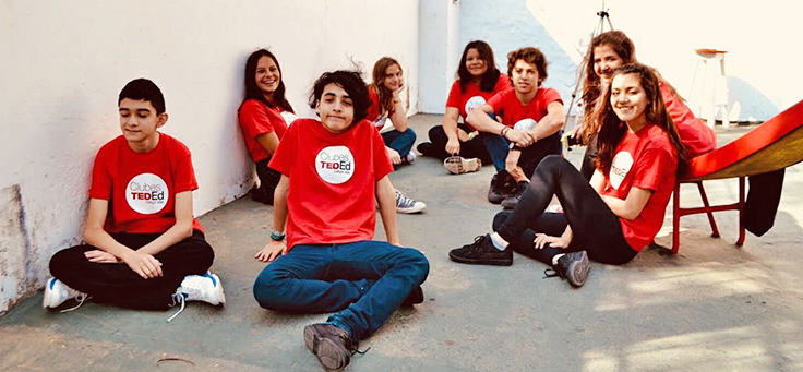 Alunos sentados em pátio escolar usando a camiseta onde se lê TED