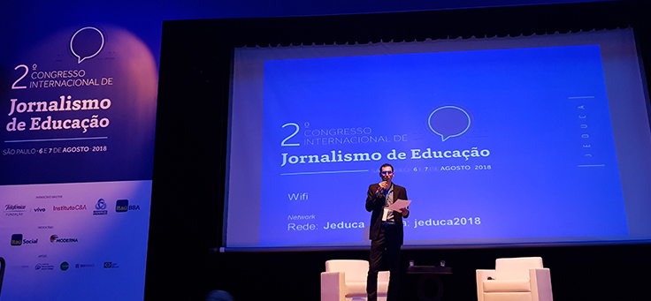 Antônio Gois, presidente do Jeduca, está em pé no palco e com microfone na mão durante a abertura do 2º Congresso Internacional de Jornalismo de Educação