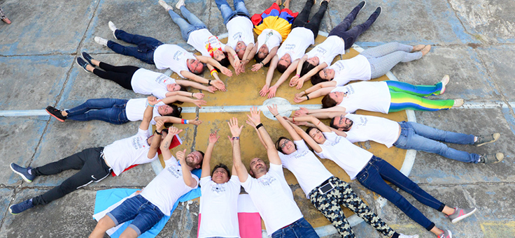 Na imagem voluntários do Vacaciones Solidárias estão deitados no chão formando um círculo, com braços e pernas esticados