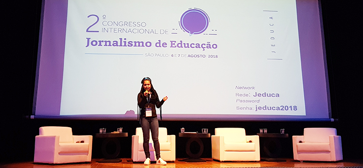 A aluna Aniely Silva está em pé no palco do Jeduca. Ela usa cabelos compridos e trançados e está com microfone na mão.