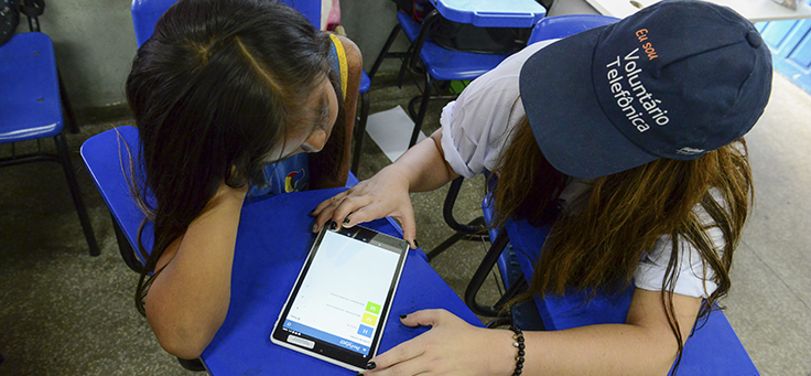 Pessoa com camiseta do Vaciones Solidarias, projeto de voluntariado internacional, usa tablete ao lado de criança