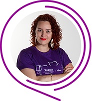 Na imagem, a voluntária Kelly Cristine Lima Fernandes posa de braços cruzados e usando camiseta púrpura do Programa de Voluntariado. Ela tem cabelos ruivos cacheados e sorri para a foto