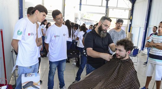 Pessoa tem cabelo cortado durante ação com trainees