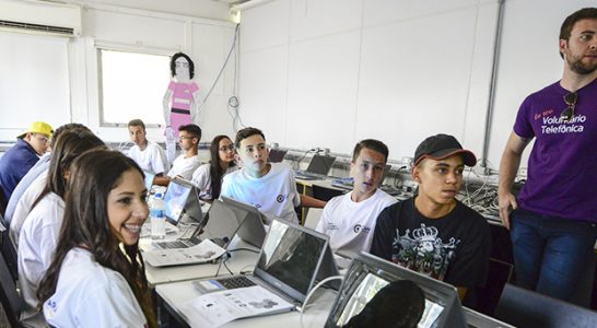 Pessoas sorriem sentadas em mesa com computadores em ação com trainees