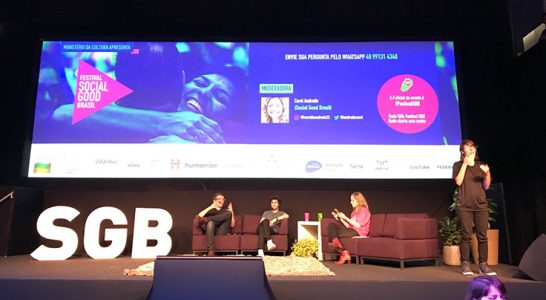 Três palestrantes dividem palco do festival Social Good Brasil. Há um intérprete de Libras, em pé