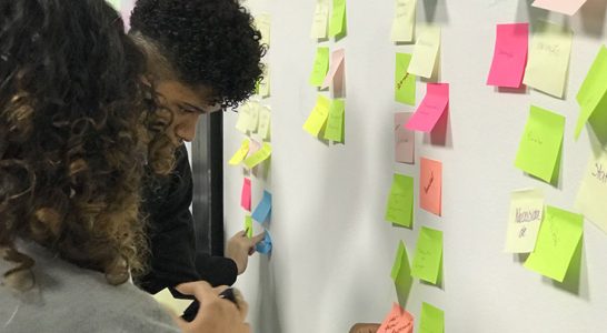Duas mulheres colam post its na parede durante dinâmica sobre metodologia da pesquisa Juventude Conectada