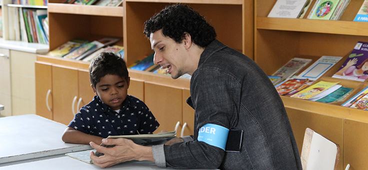 Colaborador lê livro junto com criança durante o dia dos voluntários