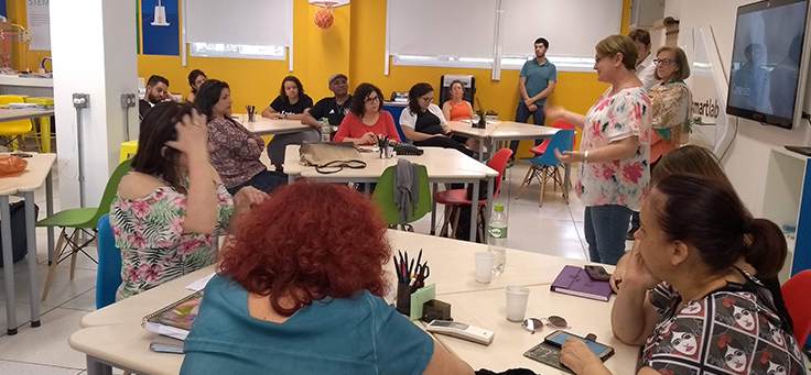 Professores estão na sala de aula, em pé e sentados, participando de uma atividade do Encontro de Integração.