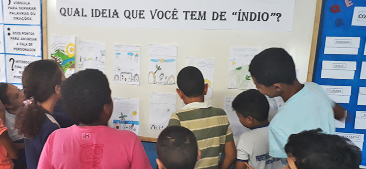 Na imagem alunos do professor Isaias olham para desenhos que mostram a visão deles sobre índios em etapa de projeto que alia leitura, tecnologia e pesquisa.