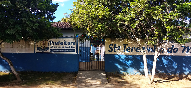 Imagem mostra muro azul e árvores em frente à Escola Municipal Santa Terezinha do Menino Jesus, onde professor criou projeto que alia leitura, tecnologia e pesquisa.