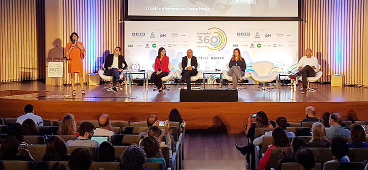 Imagem mostra Anna Penido falando ao microfone. Ao fundo estão outros palestrantes do Educação 360 STEAM, como Maria Conceição, do Sesi, e Alexsandro, do Instituto Unibanco.