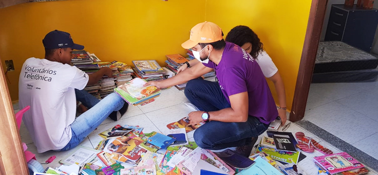Na imagem, voluntário de causas sociais usa camiseta do Programa de Voluntariado da Fundação Telefônica Vivo e auxilia a arrumar livros.