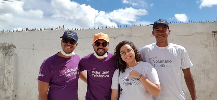 Sarlan Bernardo, que atua em diversas causas sociais, está posando ao lado de três colegas com camisetas do Dia dos Voluntários Telefônica.