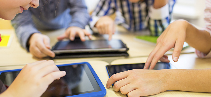 Imagem mostra três crianças sentadas em mesa e usando tablets - matéria que fala sobre ensino híbrido no Brasil foi destaque de Educação em 2018.