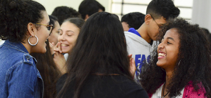 Grupo de jovens conversa, é possível ver em primeiro plano o rosto de uma menina de óculos e cabelos curtos e o de outra menina, de cabelos longos e crespos – matéria com jovens do Pense Grande foi destaque em empreendedorismo social em 2018.