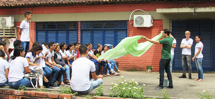 Professor Jayse Antonio, finalista do Nobel da Educação, estende pano verde em frente a seus alunos, que estão sentados em círculo no pátio da escola.