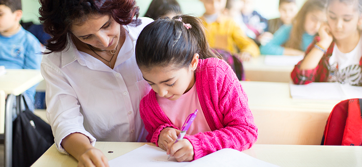 Mulher está sentada ao lado de menina, que está escrevendo. Imagem ilustra matéria sobre educação inclusiva