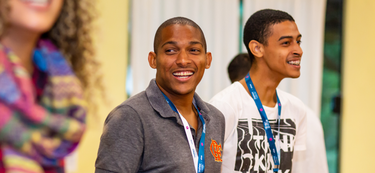 Dois jovens estão em pé, sorrindo olhando de lado para a foto. Eles participam de oficina do Pense Grande Incubação