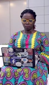 Mariéme Jamme, uma das representantes de mulheres poderosas, está com um computador no colo, usando um vestido colorido em azul, amarelo e roxo com estampa étnica.