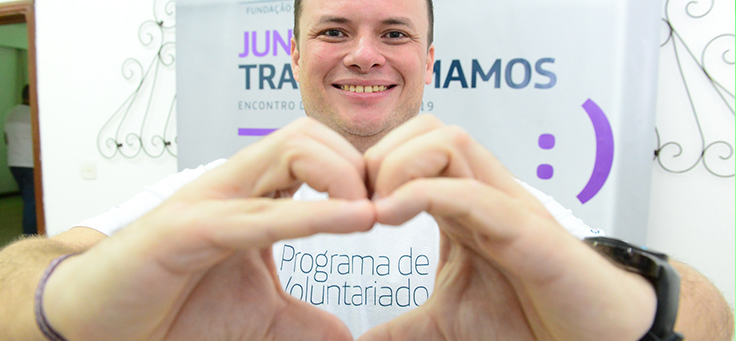 Colaborador da Fundação Telefônica Vivo está fazendo um coração com as mãos e usando uma camiseta do Programa de Voluntariado