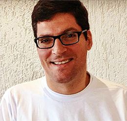 Rodrigo Hübner Mendes está usando óculos e camiseta branca e olhando para foto. O brasileiro falou em conferência anual da ONU sobre Síndrome de Down.