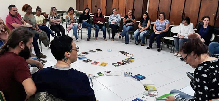 Formação de cultura de paz do Núcleo de Educação para Paz (NEP) mostra pessoas sentadas em carteiras formando um círculo em uma sala de aula.