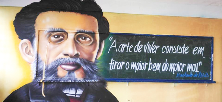 Imagem do escritor Machado de Assis, usando óculos, barba e cavanhaque estampa uma das paredes de escola em Guarulhos no projeto Grafite na Escola.