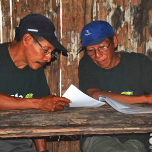 Dois xamãs da tribo Matsés dividem uma mesa e revisam enciclopédia medicinal, elaborada em parceria entre os indígenas e a ONG Acaté.