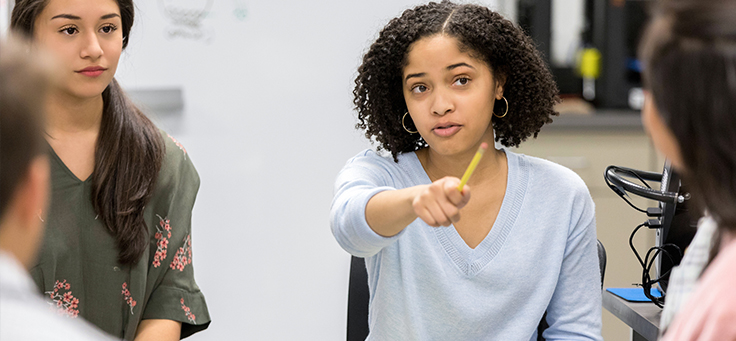 Imagem mostra uma jovem com uma mão levantada, na qual segura um lápis, participando de discussão em aula. Mudança climática é um tema que pode mobilizar jovens em sala de aula.