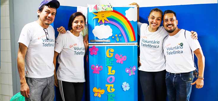 Colaboradores posam ao lado de quadro com arco-íris desenhado na Escola Municipal de Ensino Fundamental Frei Fernando, que recebeu o programa de voluntariado Vacaciones Solidárias.