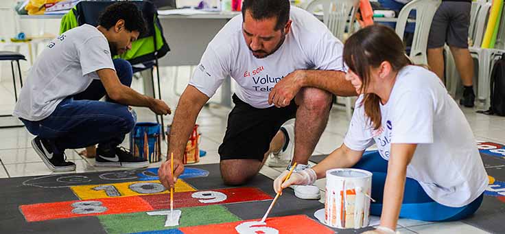 Colaboradores usam pincéis para pintar amarelinha no chão da Escola Municipal de Ensino Fundamental Frei Fernando, que recebeu o programa de voluntariado Vacaciones Solidárias.