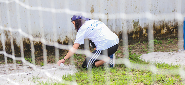 Voluntária está pintando com spray o chão do pátio da Escola Municipal de Ensino Fundamental Frei Fernando, que recebeu o programa de voluntariado Vacaciones Solidárias.