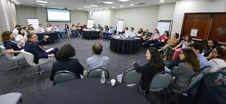 Integrantes da rede do Escola Digital estão sentados em roda conversando com especialistas, em meio a charts e um telão, durante o encontro ocorrido em São Paulo.