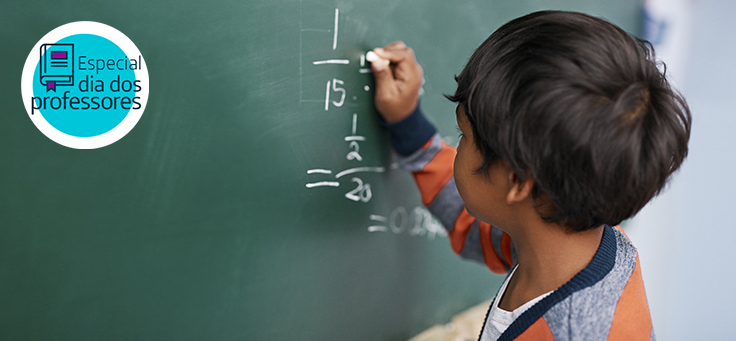 Imagem mostra menino escrevendo números com giz em uma lousa durante uma aula de matemática.