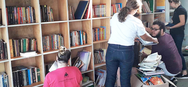 Imagem mostra pessoas arrumando livros na estante do espaço da bbiblioteca comunitária Mundo da Lua