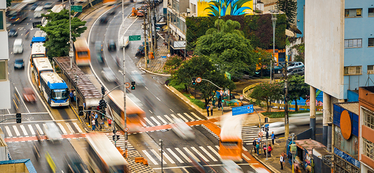 Na imagem ônibus e carros aparecem desfocados em ruas de São Paulo para ilustrar iniciativas voluntárias que transformam a vida na cidade.