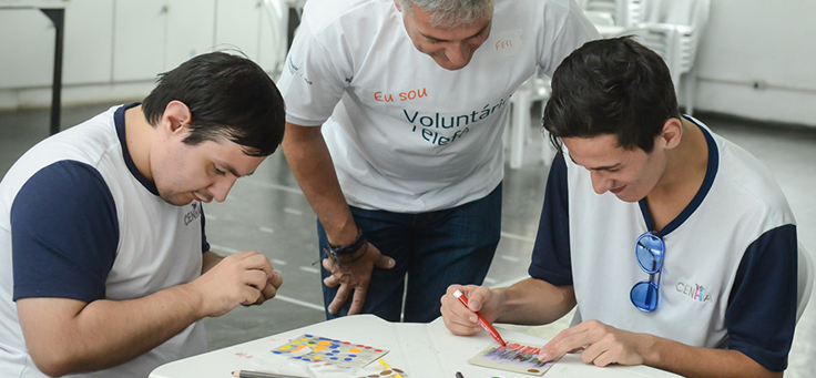 Homem está orientando jovens em atividade no CENHA, onde voluntários do Vacaciones Solidárias ensinaram programação para pessoas com deficiência intelectual.