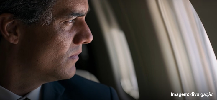 Imagem mostra cena do filme Sérgio em que aparece o ator Wagner Moura interpretando o personagem principal. Ele parece estar dentro de um avião, olhando pela janela
