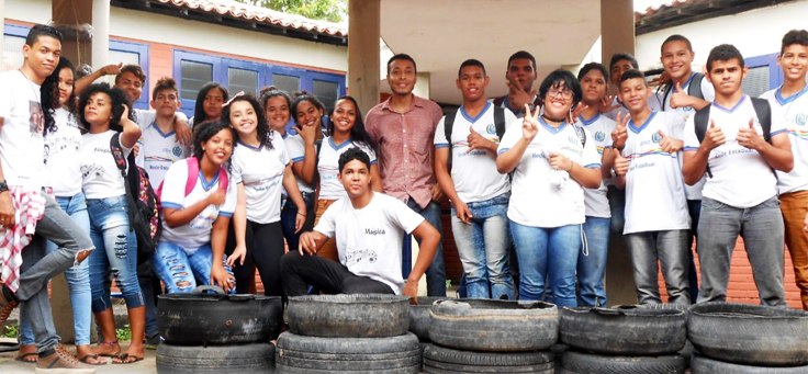 Na imagem, um grupo de alunos de uniforme posa para foto em grupo junto ao professor deles