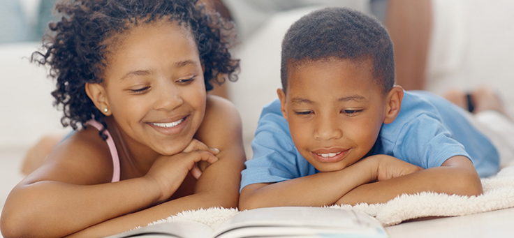 Imagem mostra duas crianças deitadas olhando para um livro