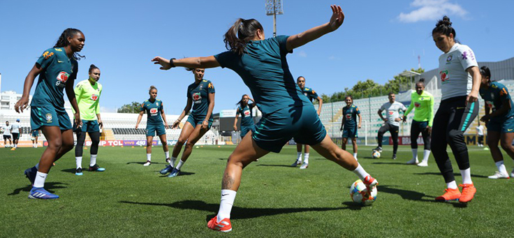 Mulheres formam roda em atividade com bola em campo de futebol no Programa de Oportunidades e Direitos, que contribui para formação de jovens.